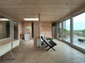 A spacious room with a large window, a radiator, a sofa, and a wooden floor. - Architect-designed cabin at Holmetangen (Vesterøy)