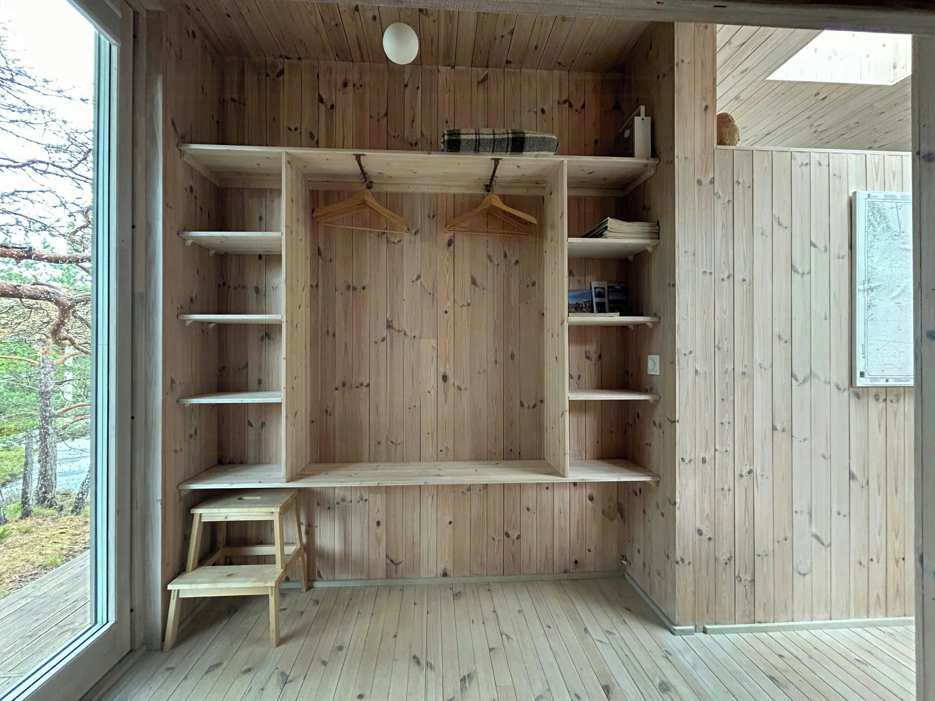 Ein Zimmer mit Holzboden, eingebauten Regalen, einer Kleiderstange und einem kleinen Tisch.