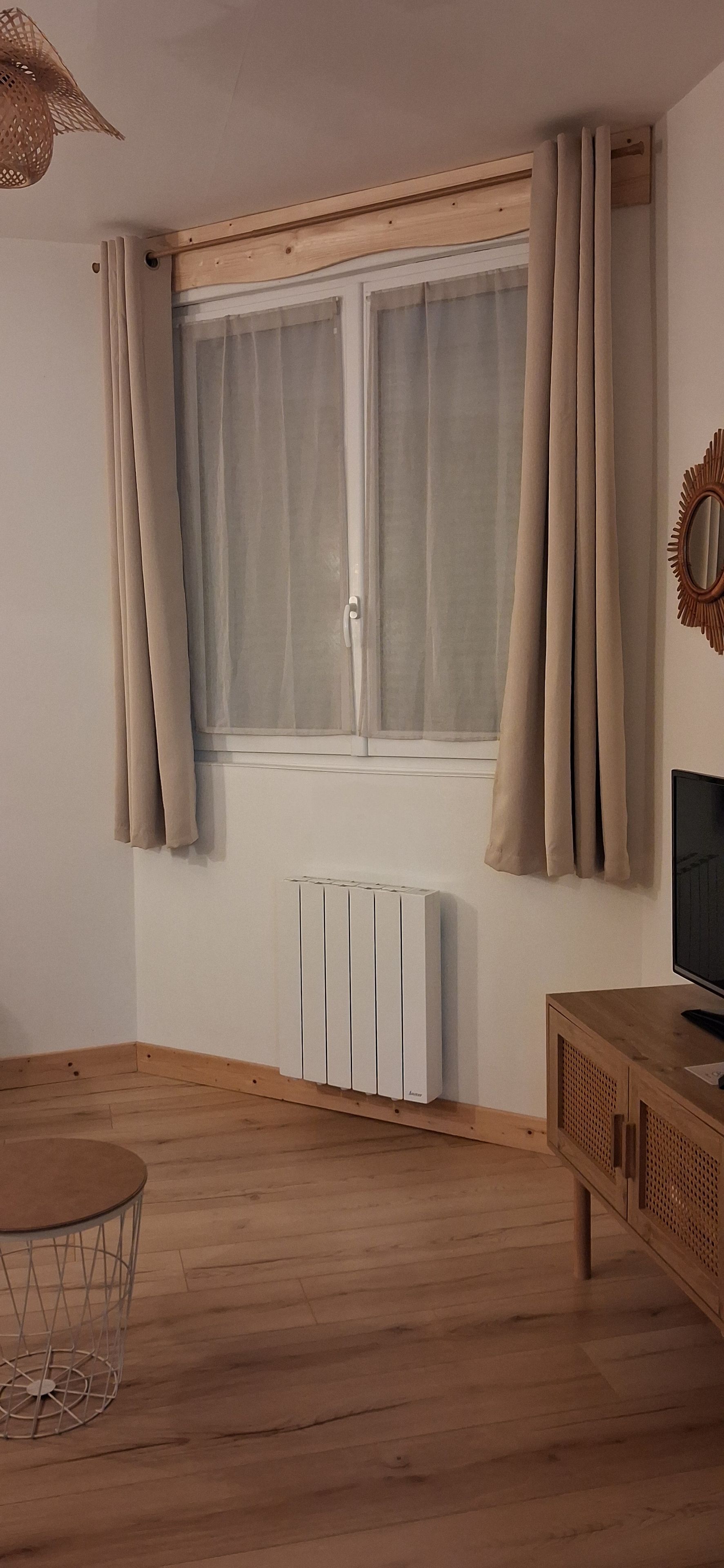 Een kamer met een raam, gordijnen, een radiator, een televisie en een houten kast.