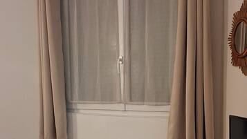 Een kamer met een raam, gordijnen, een radiator, een televisie en een houten kast.