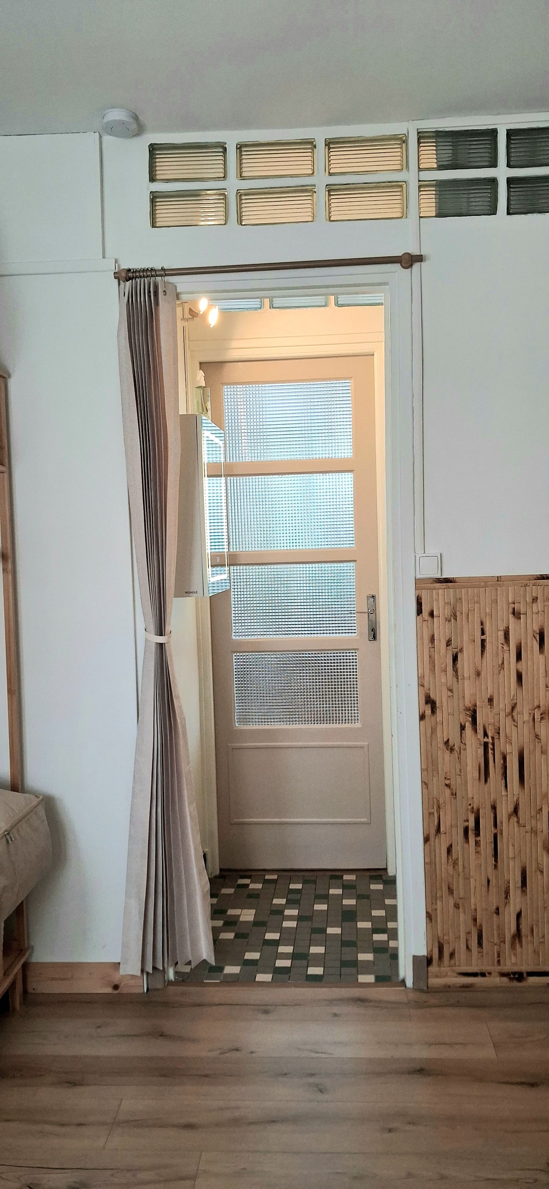 Een kamer met een houten vloer, een deur met een raam en een gordijn.
