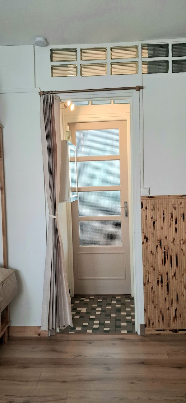 A room with a wooden floor, a door with a window, and a curtain.