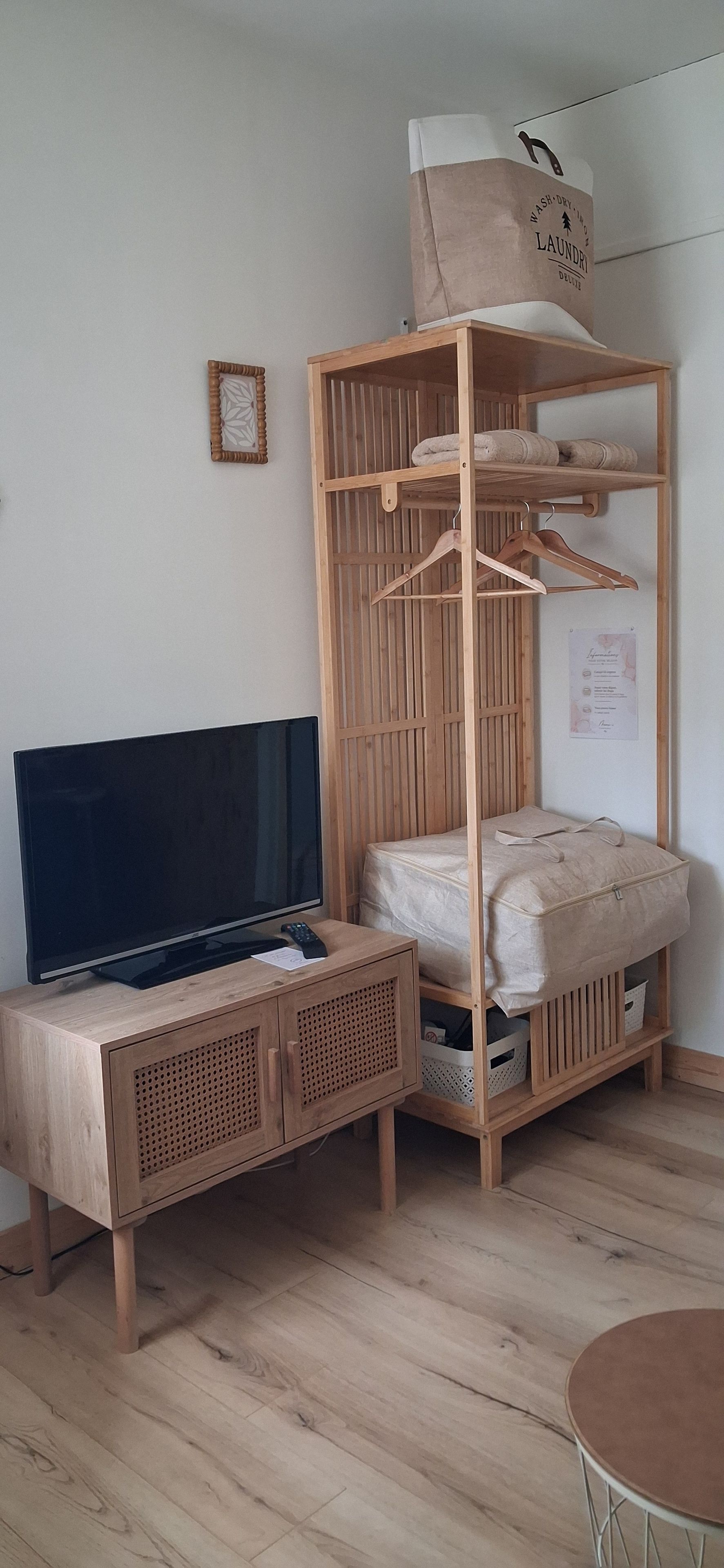 Une pièce avec un lit superposé en bois, un téléviseur posé sur un meuble en bois, une petite table et un panier à linge suspendu.