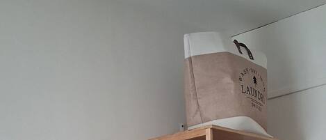A room with a wooden bunk bed, a television on a wooden stand, a small table, and a hanging laundry basket.