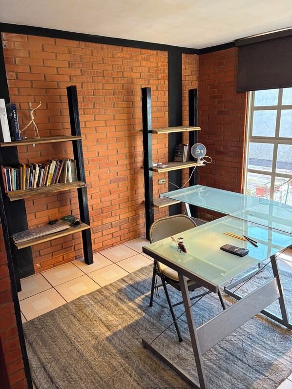 A room with a brick wall, a glass table, and a bookshelf.