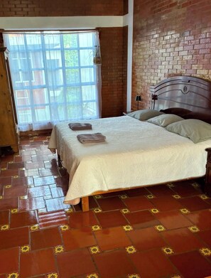 A bedroom with a large bed, a brick wall, and a window with curtains.