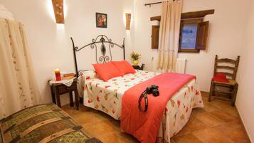 Un dormitorio con cama, mesita de noche, silla, un cofre de madera y ventana con cortinas.