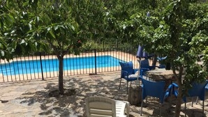 Uma área de piscina com um terraço de pedra, cadeiras azuis e uma espreguiçadeira branca.