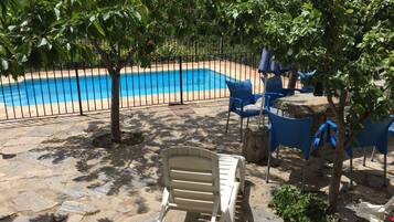 Un área de piscina con patio de piedra, sillas azules y una silla de lounge blanca.