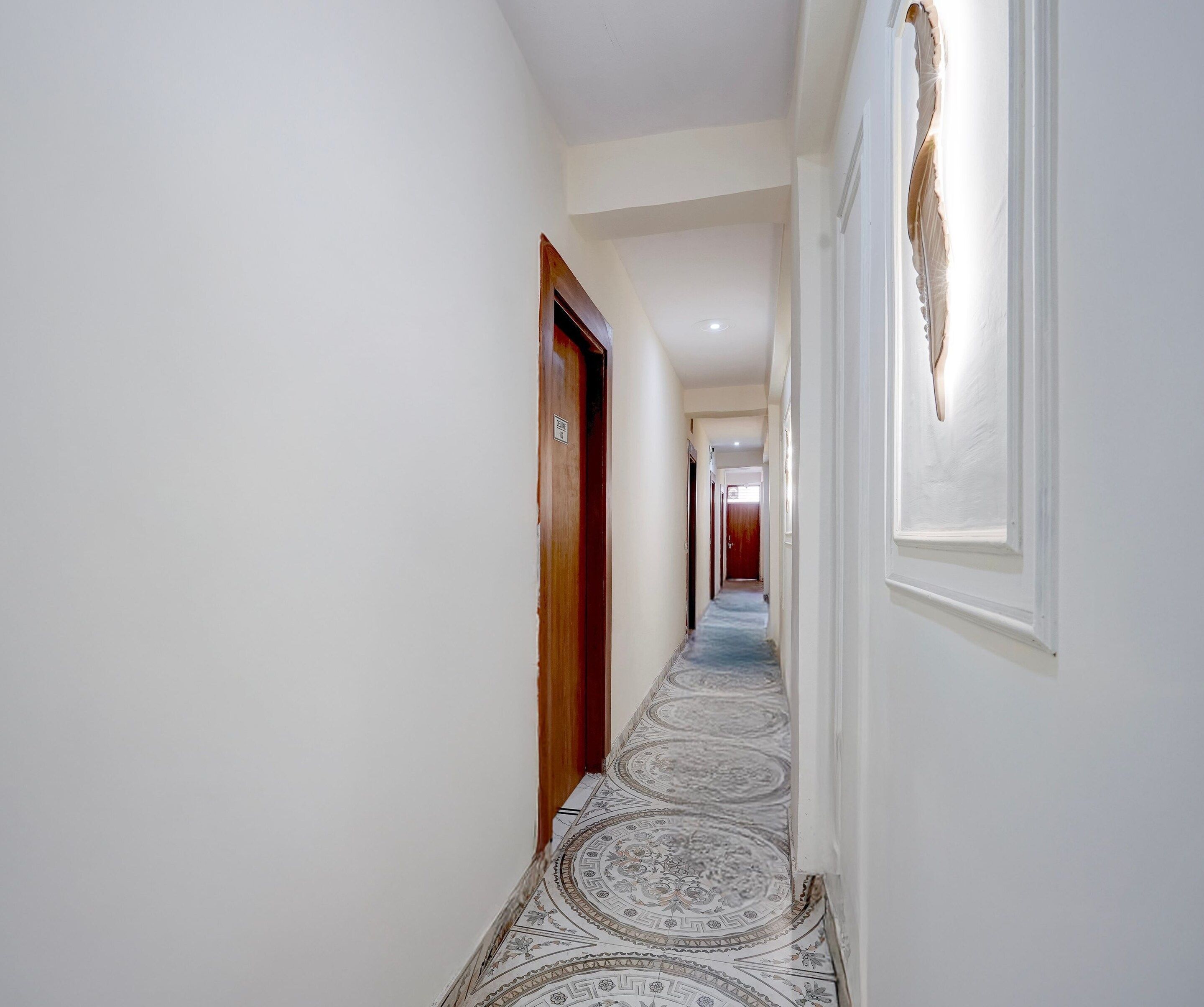 A hallway with patterned flooring, a wooden door, and a wall-mounted light fixture.