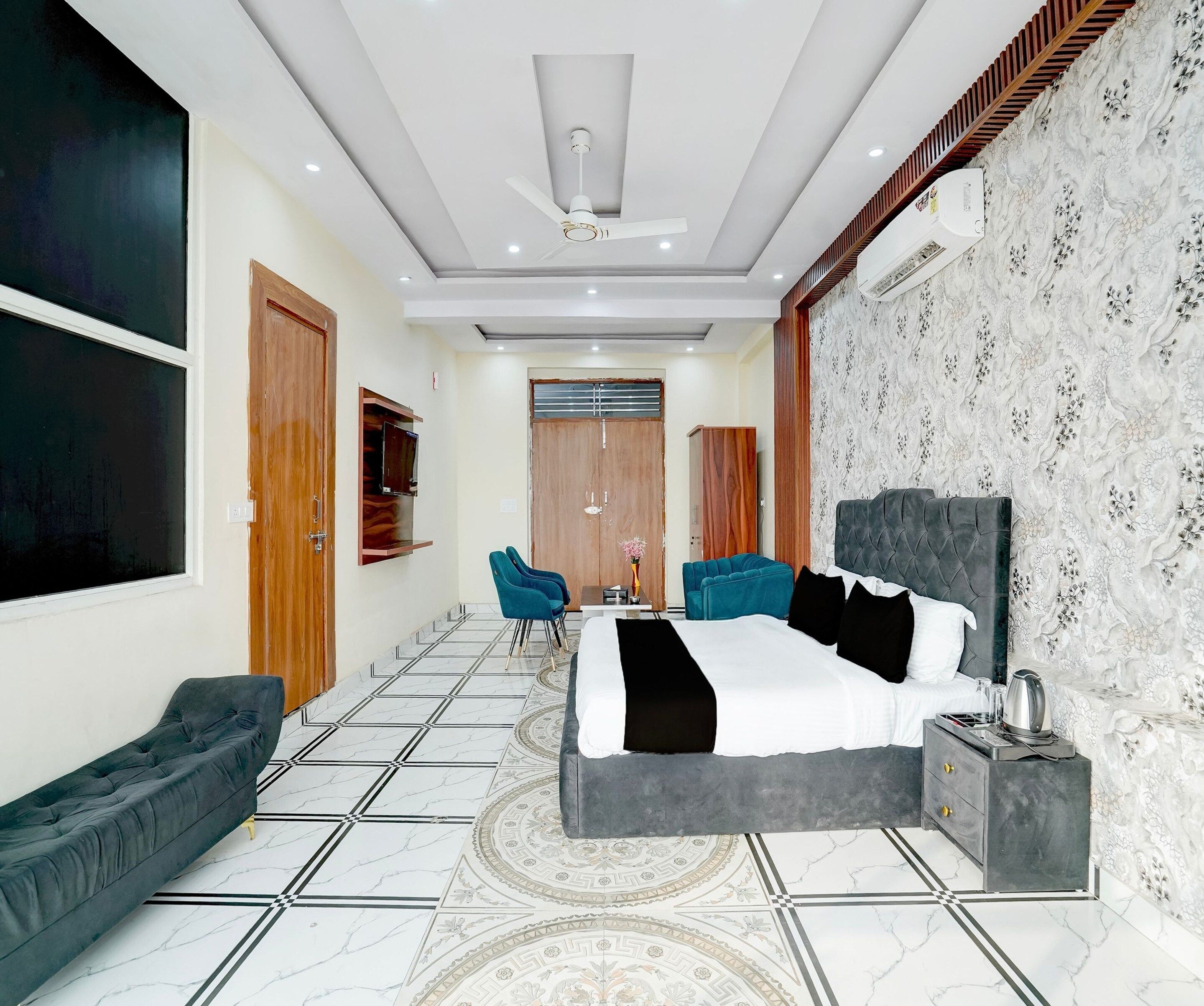 A hotel room with a large bed, two armchairs, a TV, and a ceiling fan.