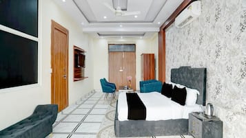 A hotel room with a large bed, two armchairs, a TV, and a ceiling fan.