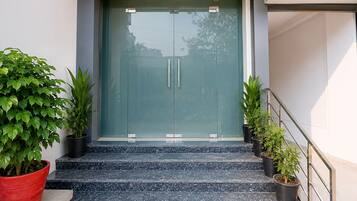 A modern building entrance with a glass door, a set of marble stairs, and potted plants.