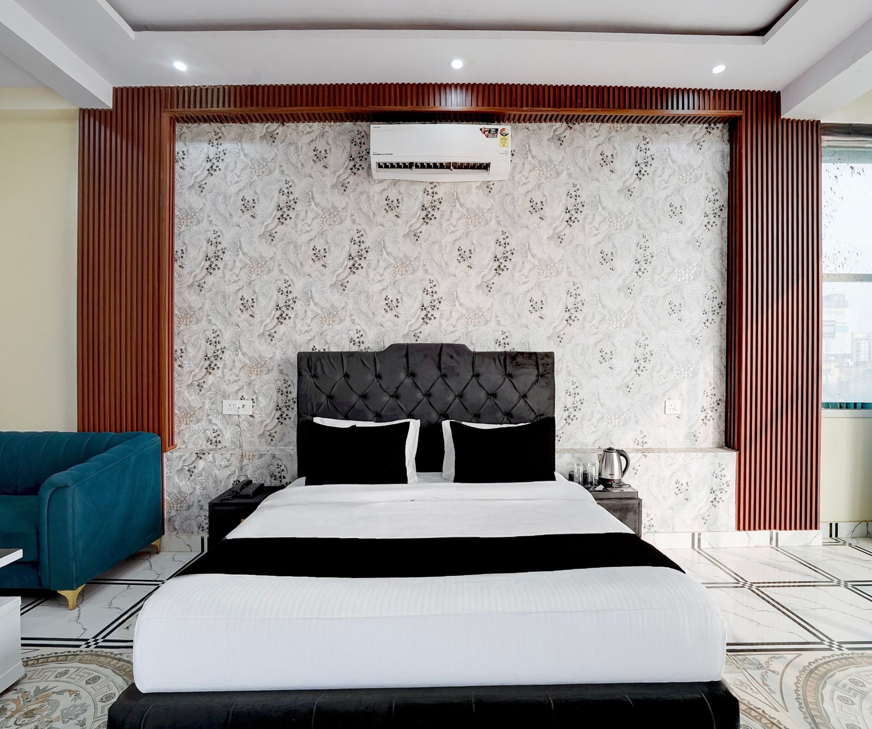 Une chambre à coucher moderne avec une tête de lit capitonnée, un grand lit avec une literie noire et blanche, un fauteuil bleu et un panneau décoratif mural.