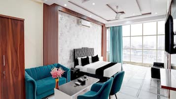 A modern hotel room with a large bed, a sofa, a coffee table, and a TV.