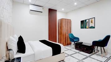 A hotel room with a bed, a desk with a coffee machine, a wardrobe, a blue chair, and a wall with framed artwork.