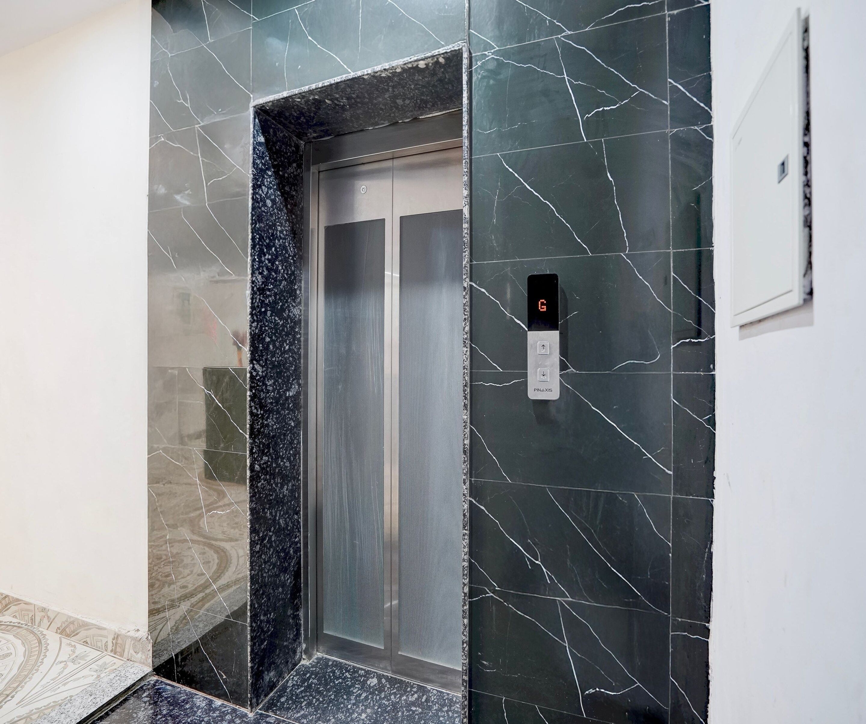 An elevator with a digital display, marble walls, and a patterned floor.