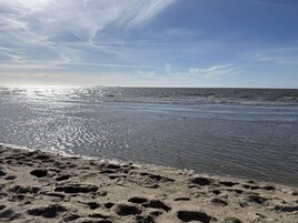 A beach with footprints in the sand and a calm sea.