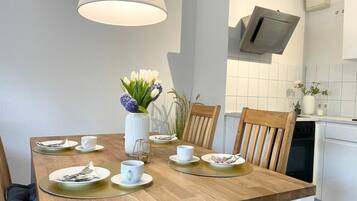 Un comedor con una mesa de madera dispuesta para cuatro personas, un florero con flores y una cocina moderna al fondo.
