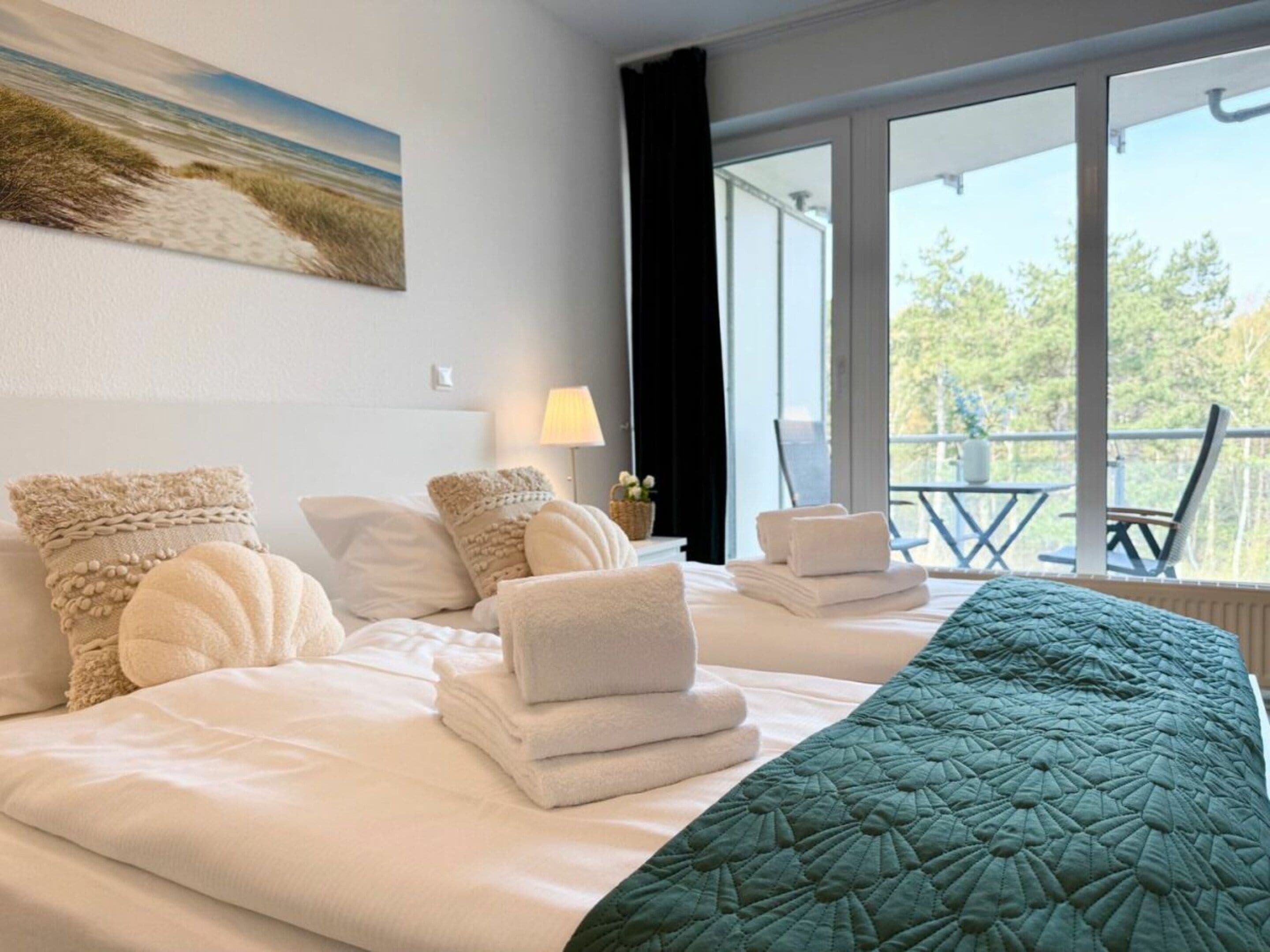 Een hotelkamer met een bed, kussens, een sprei, een raam met uitzicht op bomen en een schilderij aan de muur.