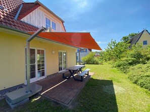 Ein Haus mit einer Terrasse, einem Tisch und einer Bank.