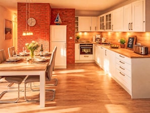 Eine moderne Küche mit Backsteinwand, weißen Schränken und einem Essbereich mit einem Holztisch und Stühlen.