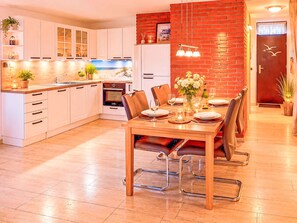 A modern kitchen with white cabinets, a built-in oven, and a dining area with a wooden table and chairs. - Albatros Royal by Interhome (Tossens)