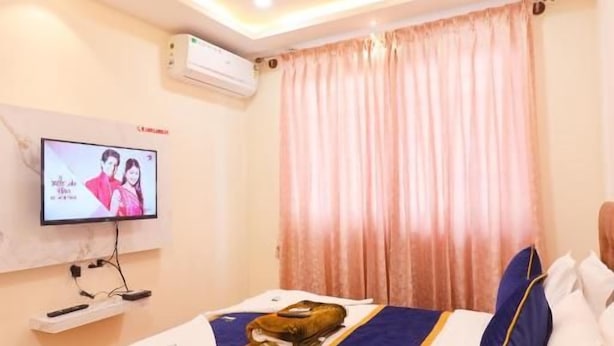 A hotel room with a bed, a television, a ceiling fan, and a window with curtains. - S V GRAND INN (Bengaluru)