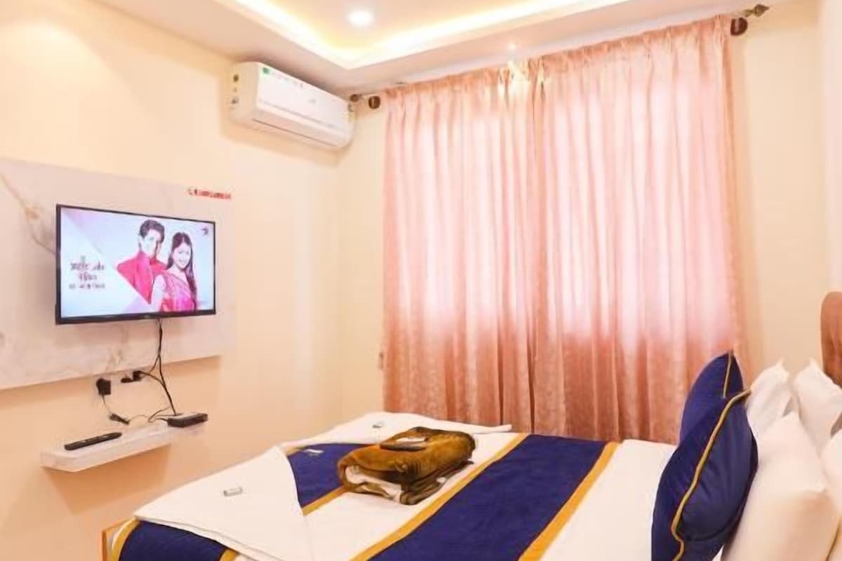 A hotel room with a bed, a television, a ceiling fan, and a window with curtains.