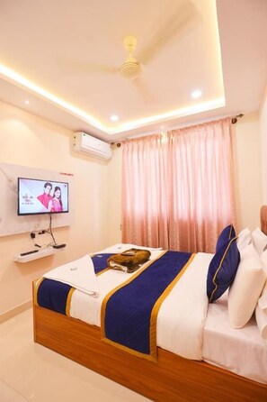 A hotel room with a bed, a television, a ceiling fan, and a window with curtains.