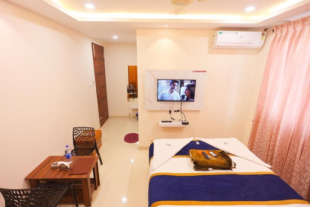 A hotel room with a bed, a TV mounted on the wall, a desk with a chair, and a window with curtains.