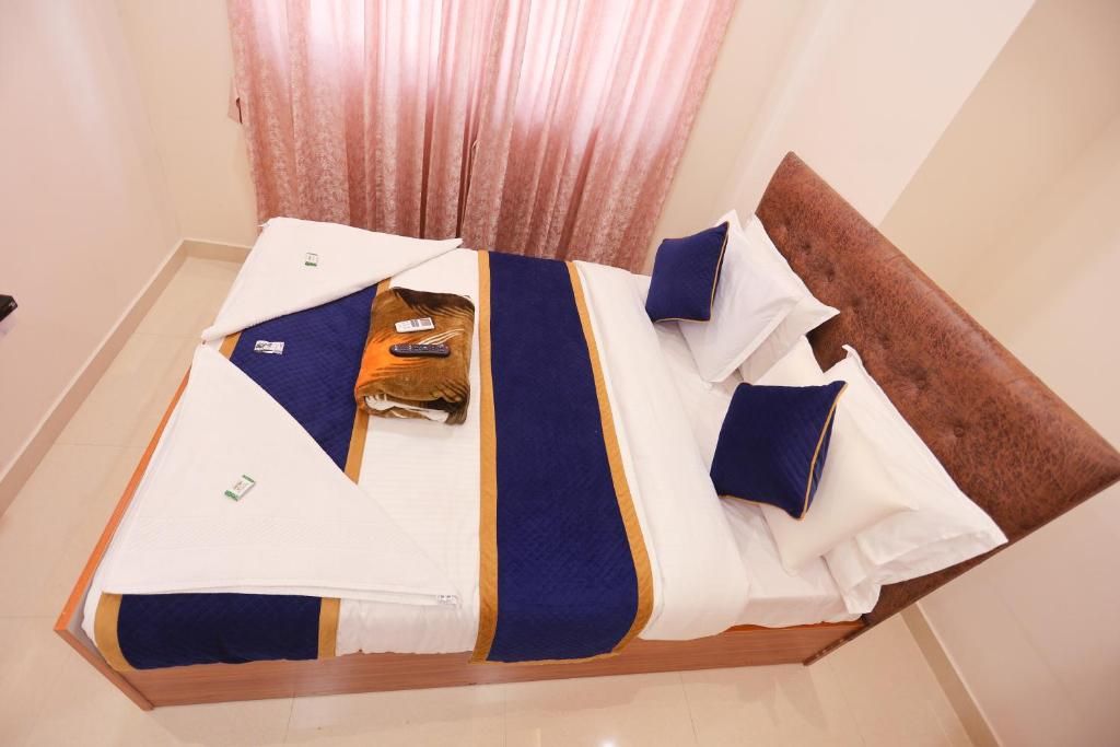 A neatly made bed with a brown headboard, white and blue bedding, and a remote control on the bed.