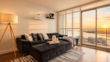 A modern living room with a dark sofa, a floor lamp, and a large window offering a city view.