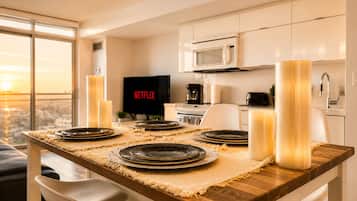 A modern dining area with a wooden table set for four, a TV displaying Netflix, and a city view through large windows.