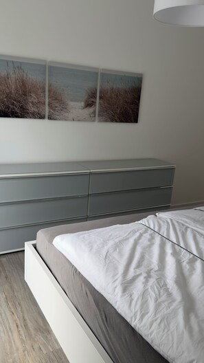 Ein Schlafzimmer mit einem Bett, einer grauen Kommode und einem Wandbild von Gras und Wasser.