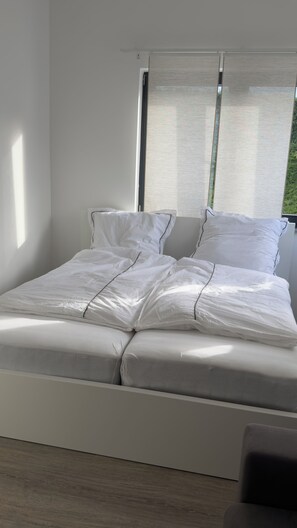 A modern bed with white linens in a room with a large window and a view of greenery outside. - Vacation Home A30 Balitherme Spa Park Heart Clinic Monteur Apartment GOP Modern (Bad Oeynhausen)