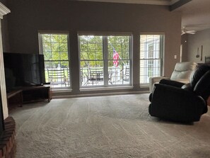 A living room with a large window, a flat-screen TV, a leather chair, and a small table.