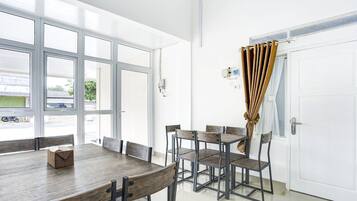 A dining area with a large table and chairs, a white door with a curtain, and a view through the windows.