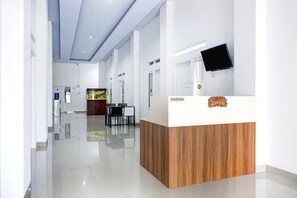 A modern reception desk with a wooden finish, a flat-screen TV mounted on the wall, and a reception area with a glass partition. - Stylish Double Suite Escape With Parking Access (Bandar Lampung)