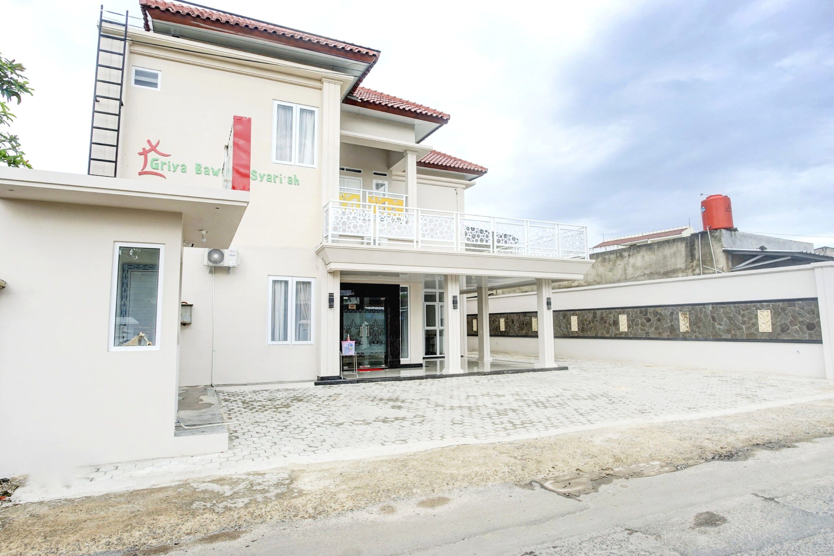 A two-story building with a balcony, a water tank on the roof, and a sign that reads 'Gria Baw Syariyah'.