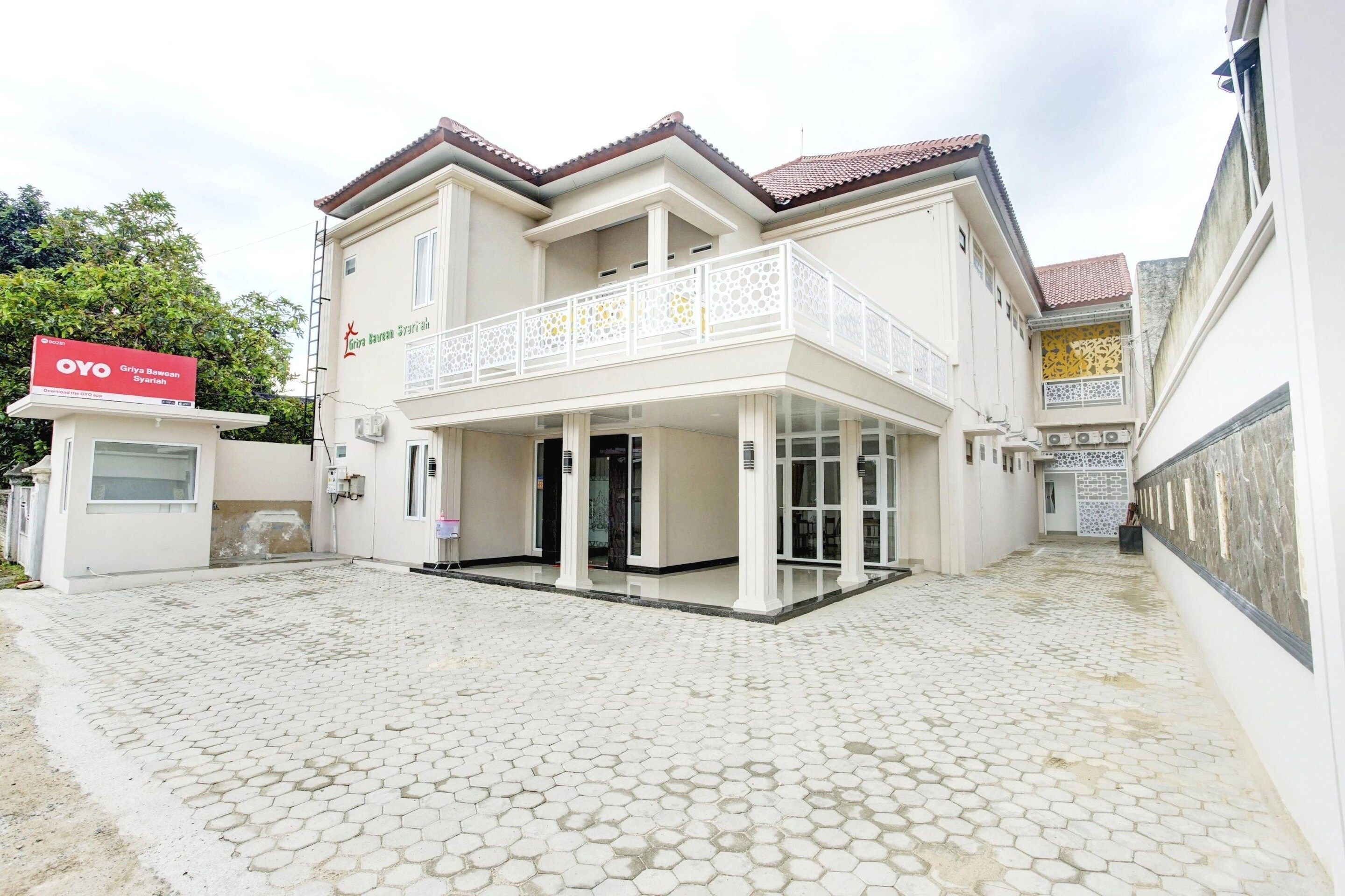 A two-story building with a balcony, a covered entrance, and a paved courtyard.