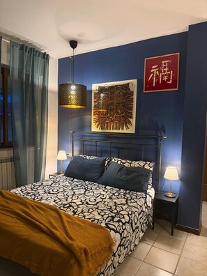A bedroom with a bed, two bedside lamps, a wall-mounted artwork, and a red sign. - Just a Stone's Throw Away – Cozy Apartment with Parking in Grosseto (Grosseto)