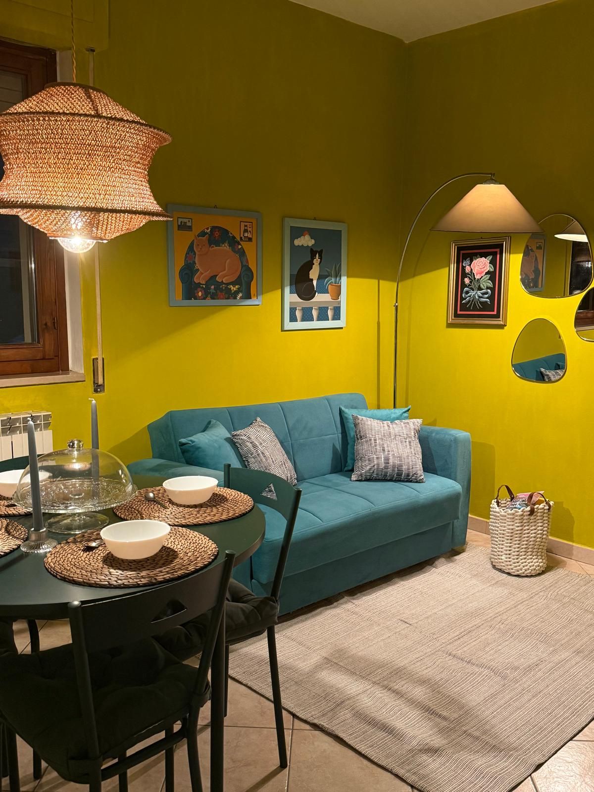 Una stanza con un divano color petrolio, un tavolo da pranzo con sottopiatti e opere d'arte alle pareti.
