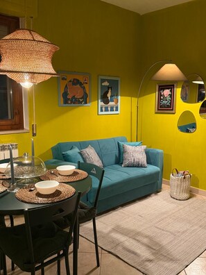 A room with a teal sofa, a dining table with placemats, and wall art. - Just a Stone's Throw Away – Cozy Apartment with Parking in Grosseto (Grosseto)