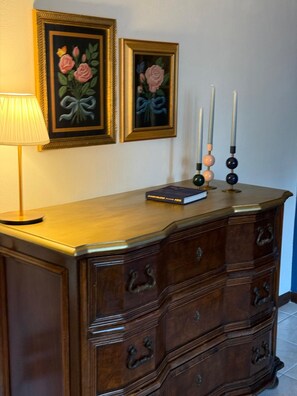 A wooden dresser with multiple drawers, a lamp, and two framed floral paintings on the wall. - Just a Stone's Throw Away – Cozy Apartment with Parking in Grosseto (Grosseto)