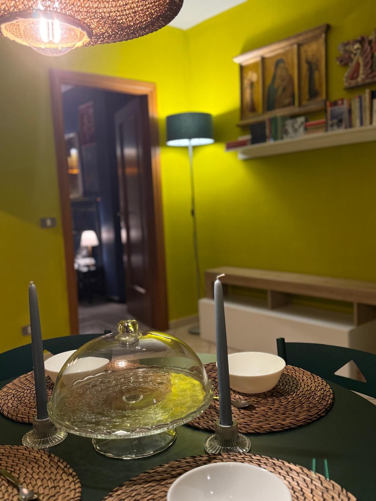 Un tavolo da pranzo con un elemento centrale in vetro, candele e sottopiatti tessuti.