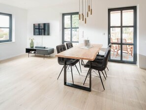 A modern dining area with a wooden table, black chairs, and a TV mounted on the wall. - Coastal Suite South Side Waterfront Location (Krummhoern)