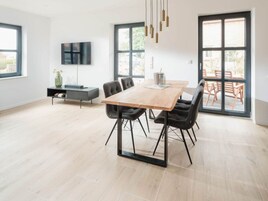 Uma área de refeições moderna com uma mesa de madeira, cadeiras pretas e uma TV fixada na parede.