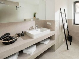 Un baño moderno con un espejo grande, un lavamanos blanco, un perchero y una escalera negra.