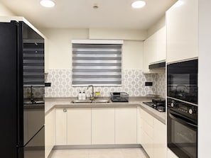 A modern kitchen with a built-in oven, a stainless steel sink, and a window with blinds.